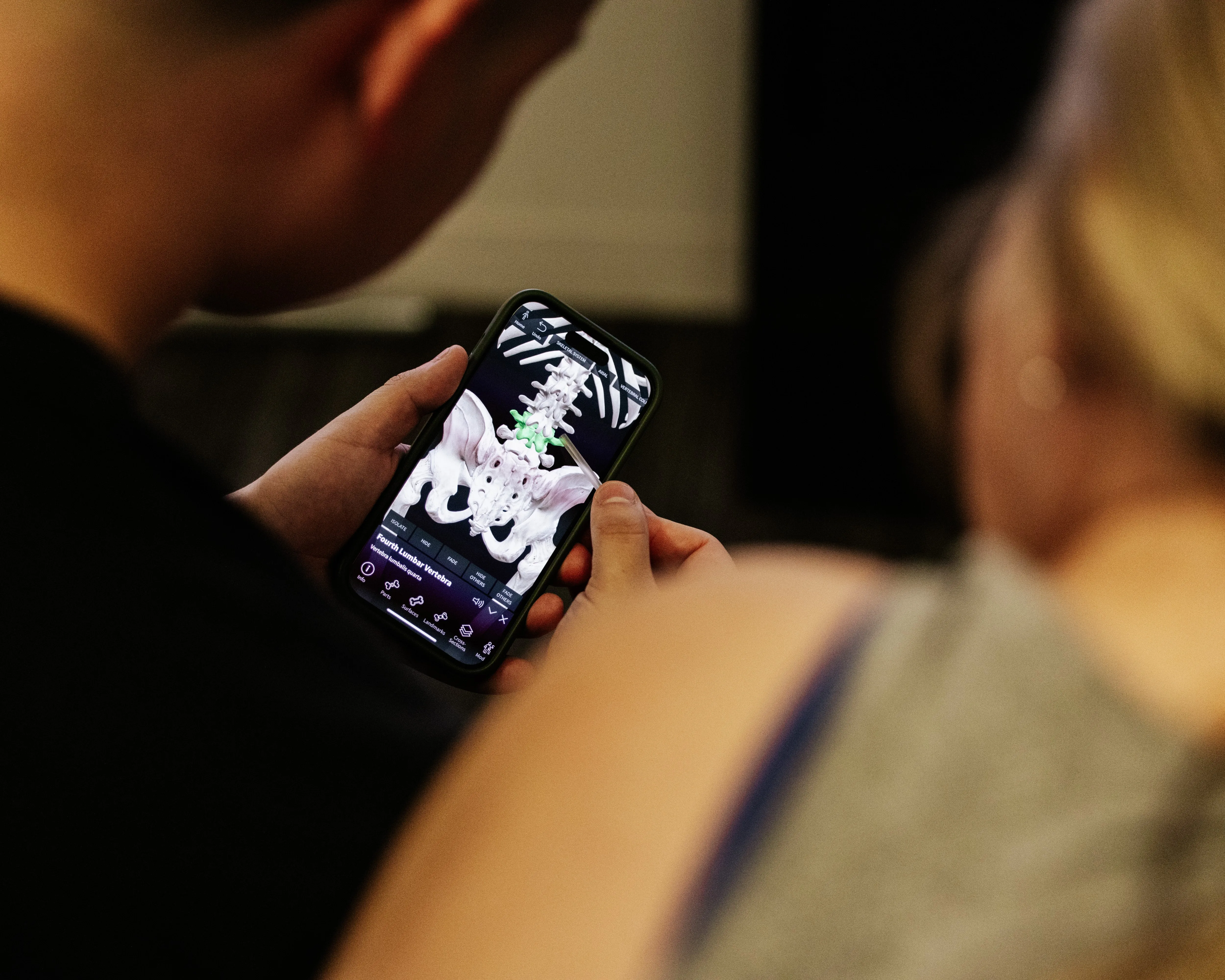 A client looks at a screen showing a human skeleton highlighting different areas of the spine.